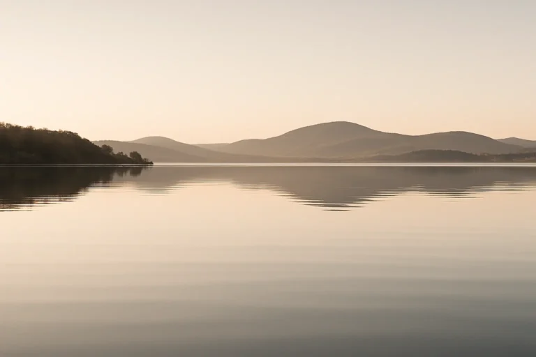 Stilles Wasser mit sanftem Licht und Bergen im Hintergrund – Symbol für Harmonie und Klarheit.