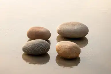 Vier natürliche Steine liegen ausgewogen in einer ruhigen Wasserfläche mit feinen konzentrischen Wellen, warmes Licht und sanfte Erdtöne im Integralux Stil.