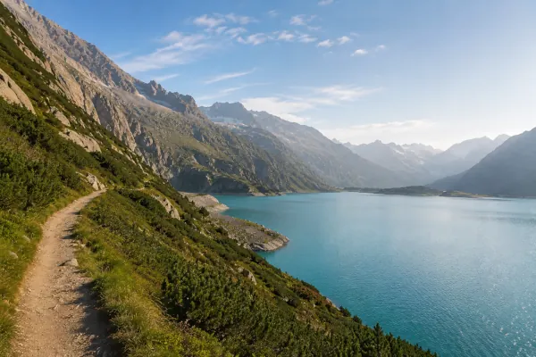 Bergpfad entlang eines türkisfarbenen Alpensees mit weiter Gebirgslandschaft im Morgenlicht als Symbol für Orientierung und Klarheit.